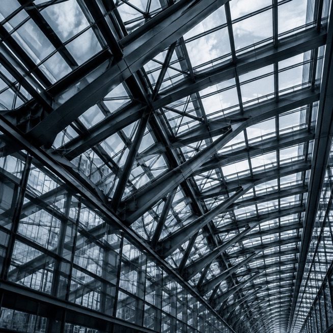 Looking up into a glass atrium roof held by a lattice of steel beams